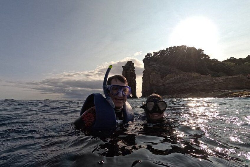 Two people snorkeling in the ocean with a rocky cliff in the background. 2
