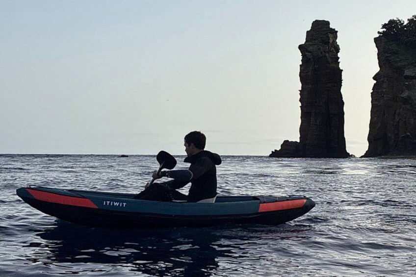 A person in a small boat on calm water with a rocky formation in the background. 4
