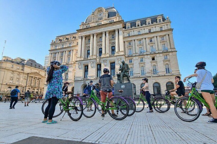 A group of people with bicycles in front of a large historic building with classical architecture. 5