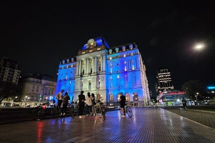A brightly lit historic building with people around it. 1