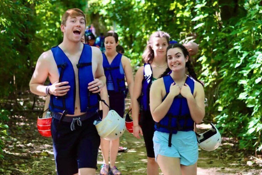 People running in a forested area, wearing blue life jackets and carrying water bottles. 3