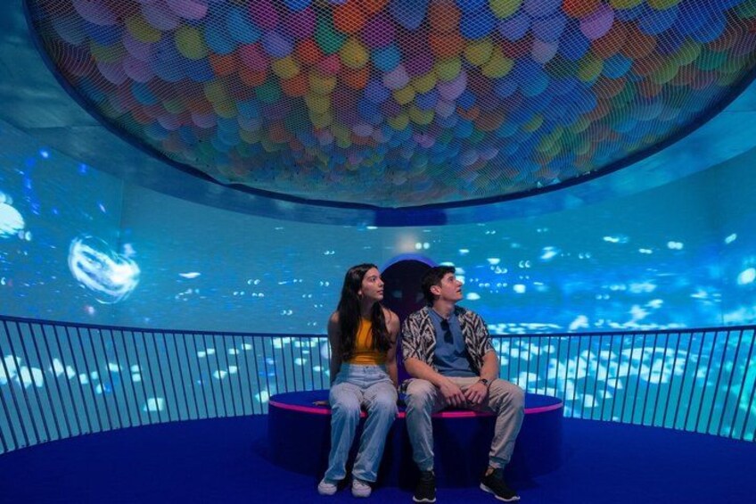 A couple sitting on a blue platform with a colorful, circular ceiling decoration. 3