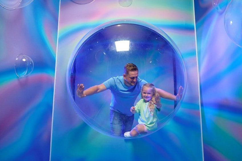 A man and a child inside a transparent spherical structure with a colorful background. 3