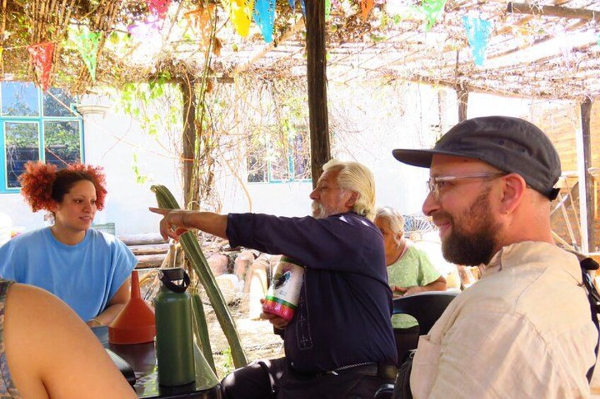 People sitting outdoors under a pergola with colorful flags, a green thermos, and a bottle. 3