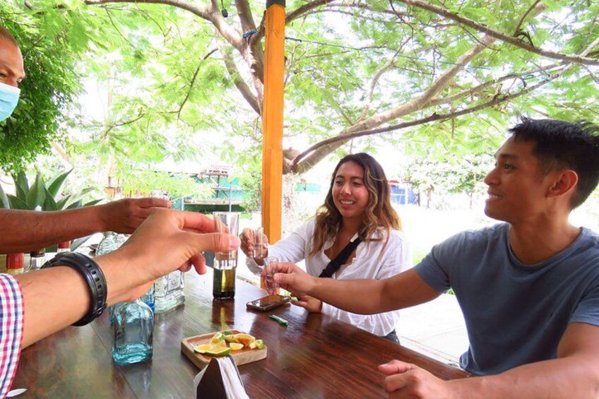 A group of people toasting with drinks at an outdoor table with a wooden surface, surrounded by greenery. 2