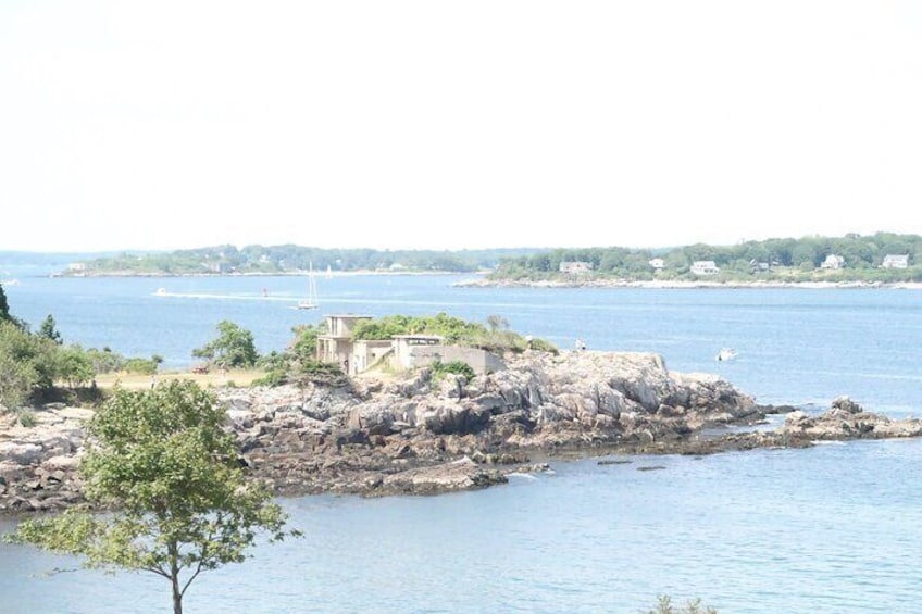 A rocky shoreline with a small building, calm water, and distant land with greenery. 5