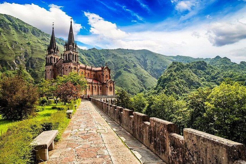 A historic church with two spires, surrounded by lush green hills and a stone pathway leading to it. 2