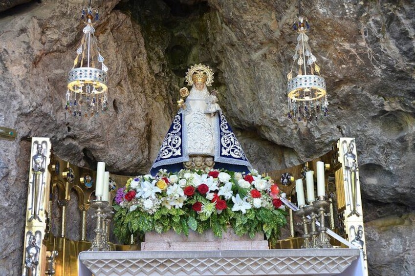 Une statue religieuse, vêtue d’une robe bleue et blanche, entourée de fleurs et de bougies, se dressant sur un fond rocheux. 4