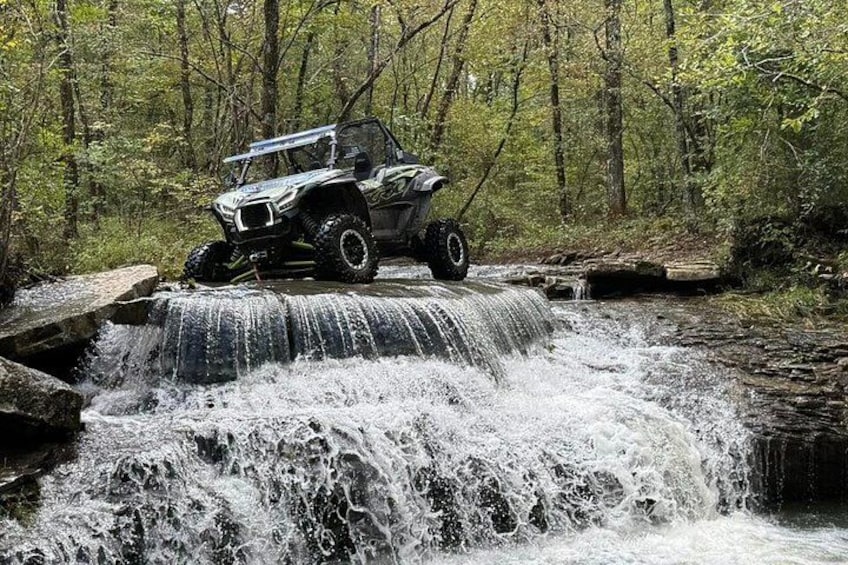 A vehicle crossing a waterfall in a forest. 1