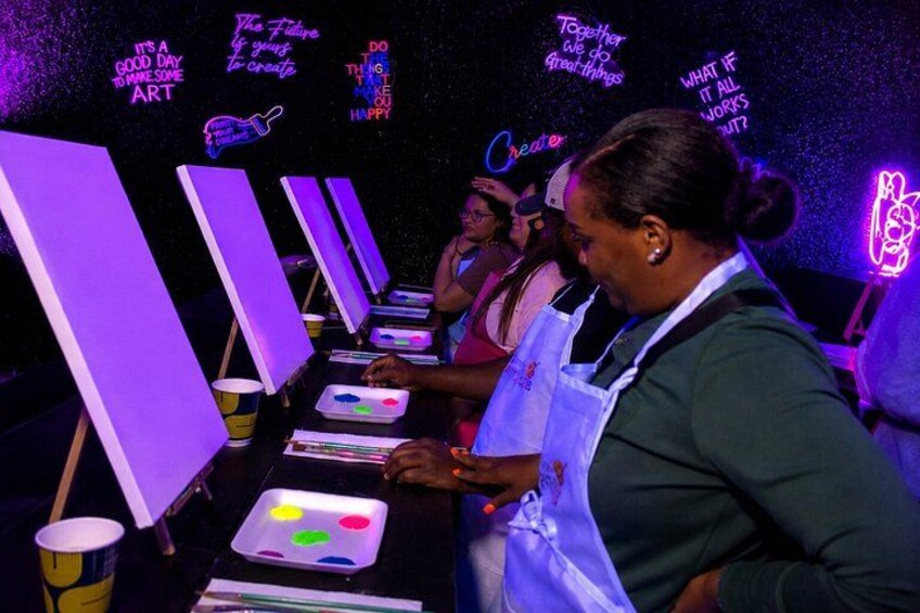 A person painting on a canvas in a room with neon signs. 4
