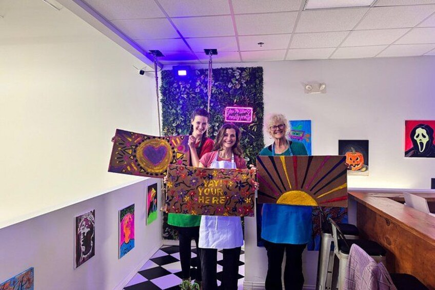 Three people holding a large, colorful sign with a heart and sun design. 4