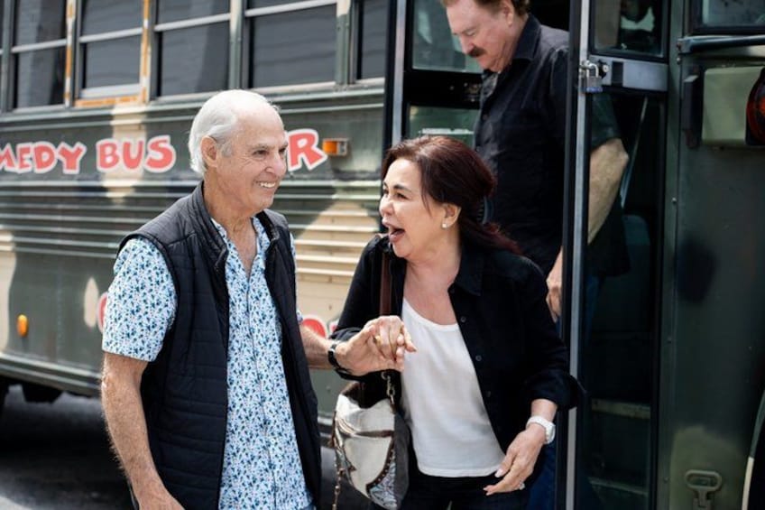 Two people standing in front of a bus with 'COMEDY BUS' written on it. 3