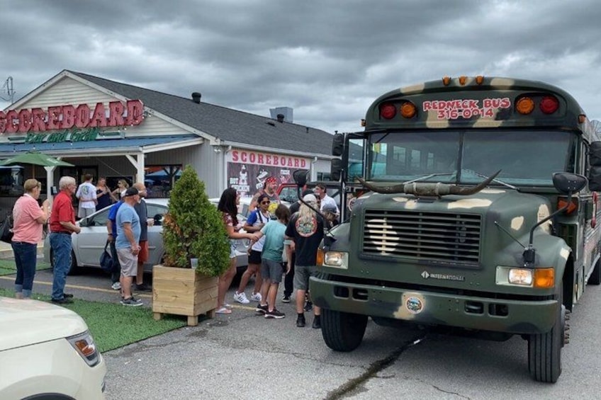 A military-style bus parked in front of a building with a sign that reads 'SCOREBOARD.' 5