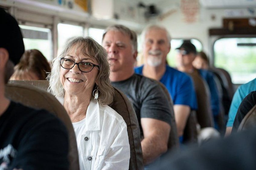 A group of people seated inside a vehicle, likely a bus or van, with windows and a visible interior structure. 5