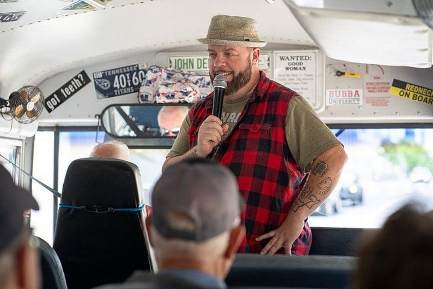 A man speaking into a microphone inside a bus with various signs and advertisements on the walls. 4