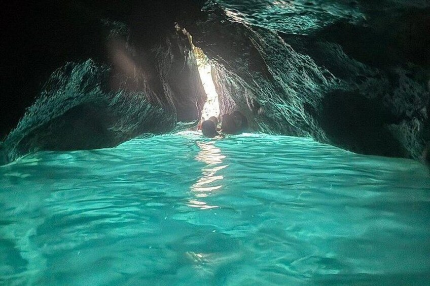A cave with clear turquoise water and a person standing in the center. 2
