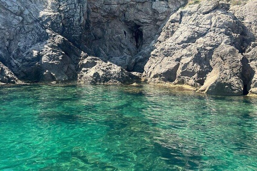 Clear turquoise water, rocky cliffs, and a cave entrance. 4