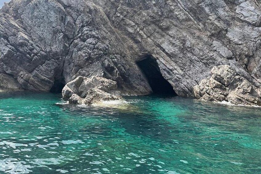 A rocky coastline with a cave entrance and clear turquoise water. 5
