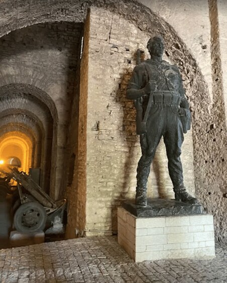 A statue of a historical figure in a stone niche, with an arched doorway and a wheel in the background. 3