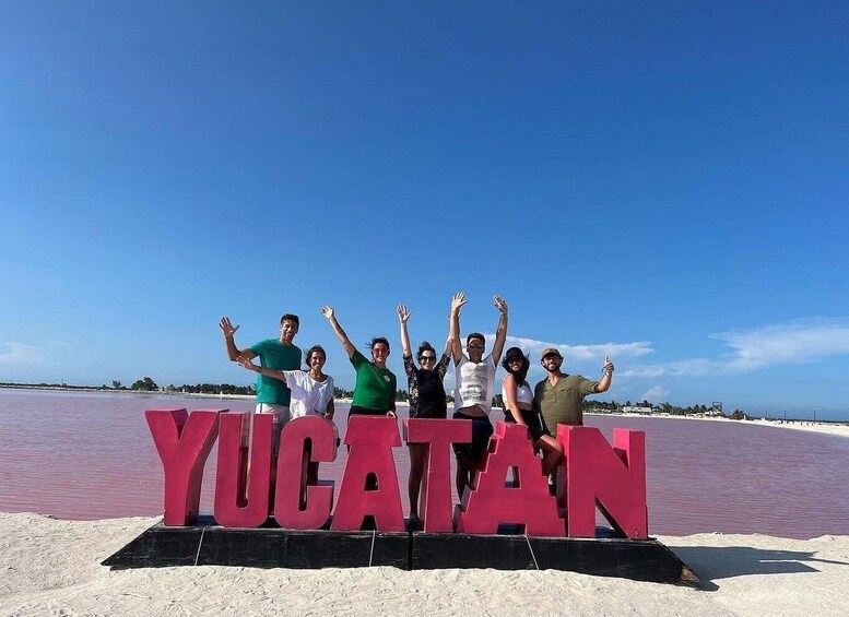 A group of people posing in front of a large 'Yucatan' sign on a beach. 5