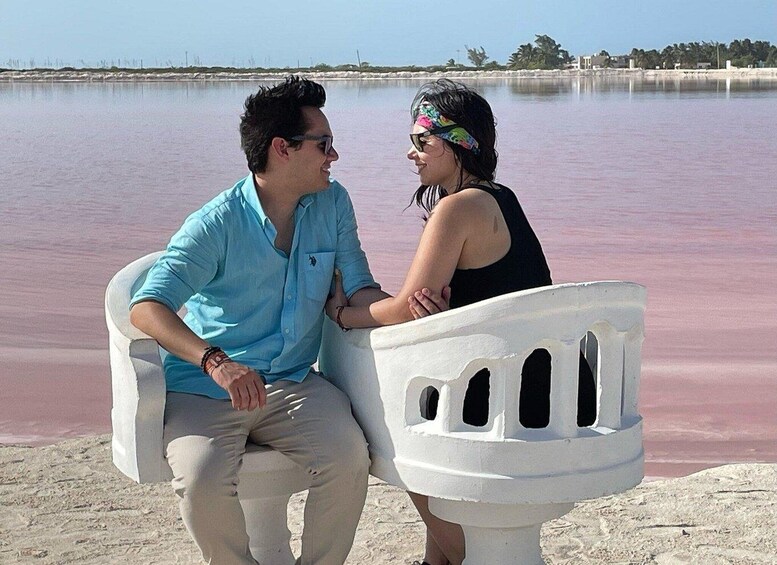Two people sitting on a white bench by a body of water with a pinkish hue. 3