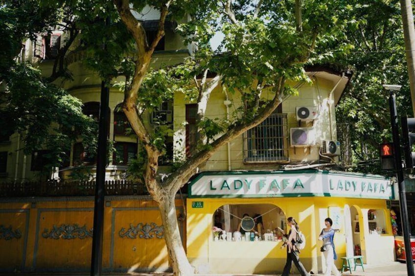 A yellow building with 'Lady Fafa' signage, a tree in front, and a person walking. 1