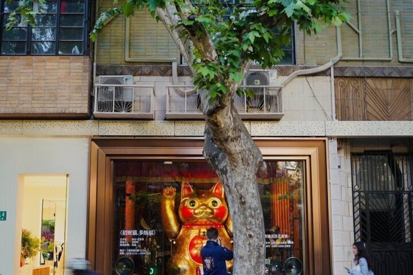 A storefront with a large golden cat statue, a tree in front, and a balcony with air conditioning units. 2