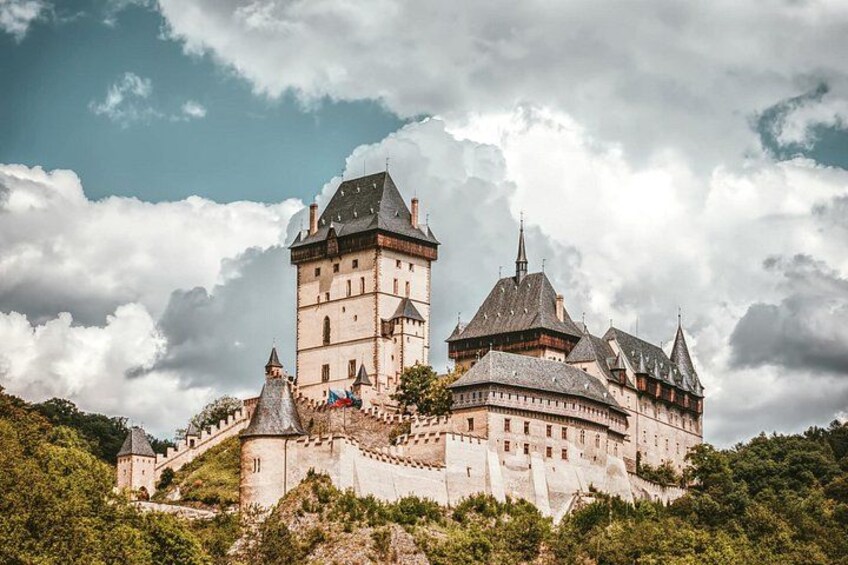 A historic castle with multiple towers, surrounded by lush greenery and a cloudy sky. 1