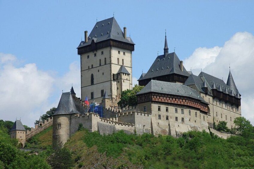 A historic castle with multiple towers, a fortified wall, and lush greenery. 2