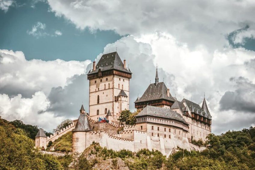A historic castle with multiple towers, surrounded by lush greenery and a cloudy sky. 1