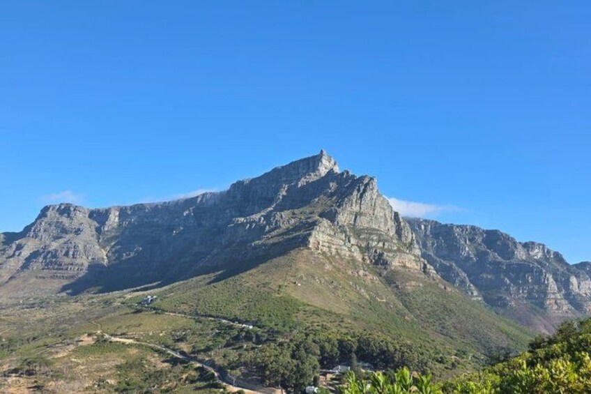 A mountain with a prominent peak, a valley with sparse vegetation, and a clear blue sky. 2