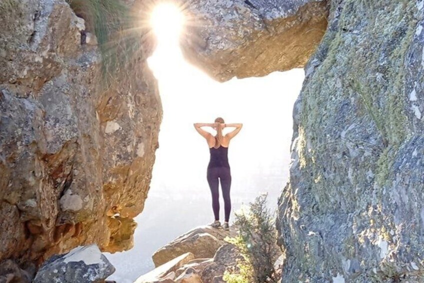 A person standing on a rock formation with a natural archway, sunlight shining through. 1