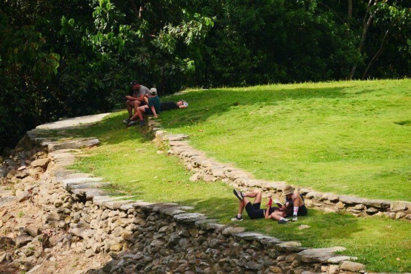 A stone wall with people sitting on the grass beside it. 1