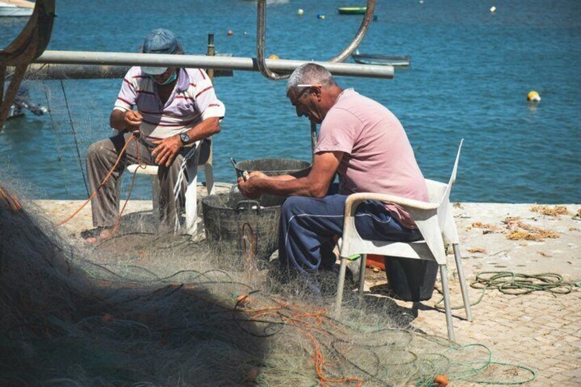 Two men sitting by a body of water, engaged in fishing activities with nets and equipment. 3