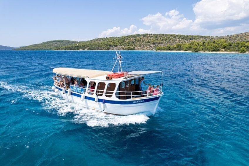 A boat with passengers on a clear blue sea, surrounded by a hilly landscape. 3