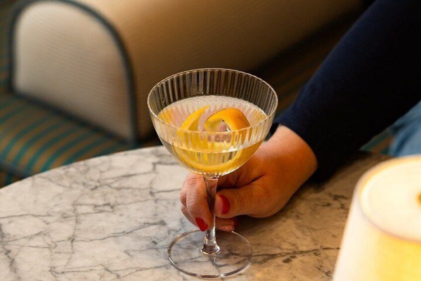 A hand holding a cocktail glass with an orange slice on a marble table. 3
