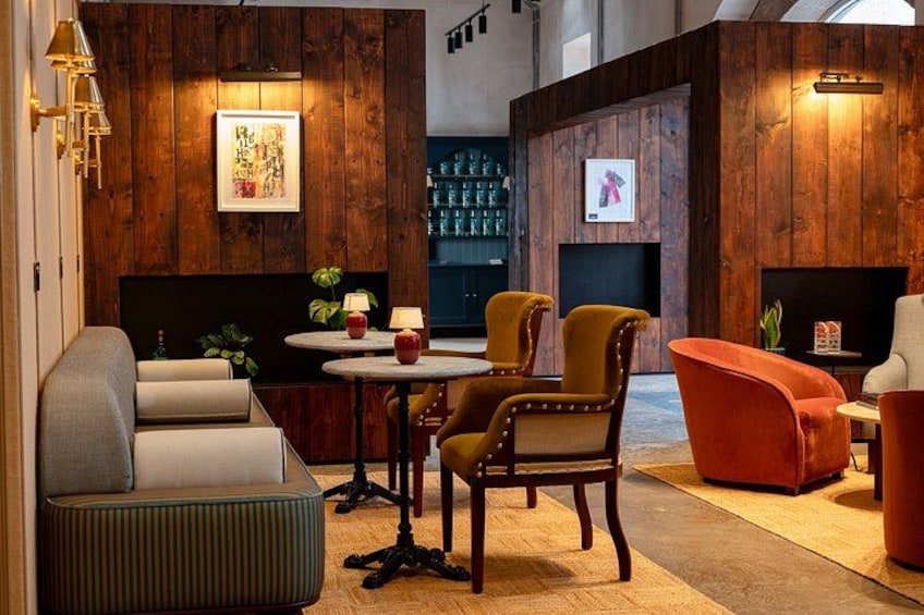 A modern lounge area with wooden panel walls, a sofa, armchairs, a small table with lamps, and a fireplace. 1