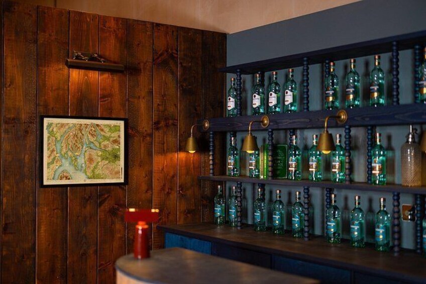 A bar with wooden walls, shelves of green bottles, a red candle, and a framed map. 5