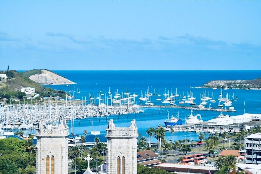 A coastal marina with numerous sailboats, a prominent stone tower, and a clear blue sky. 1