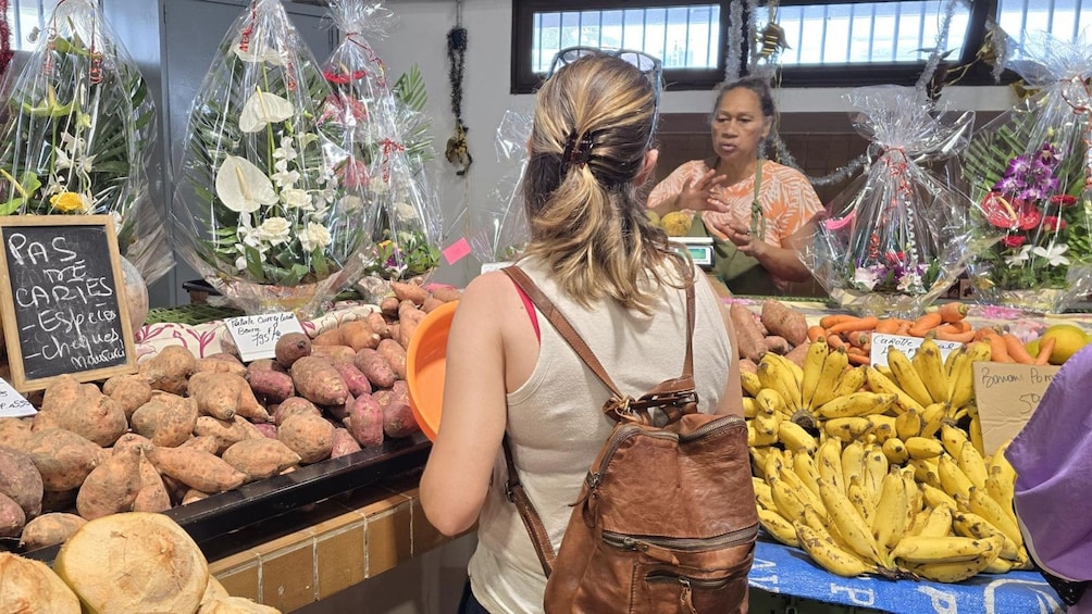A market stall with sweet potatoes, bananas, and flowers. 2