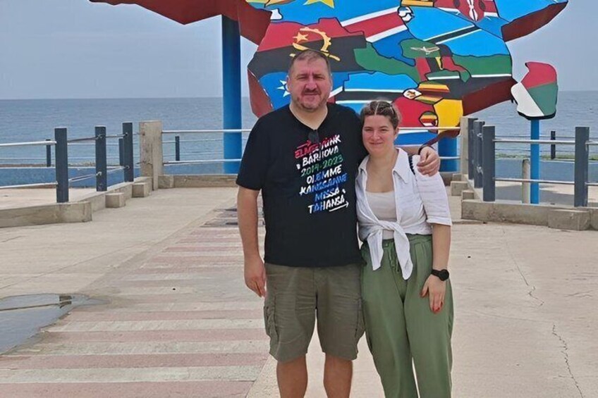 Two people standing in front of a colorful mural with a coastal background. 3