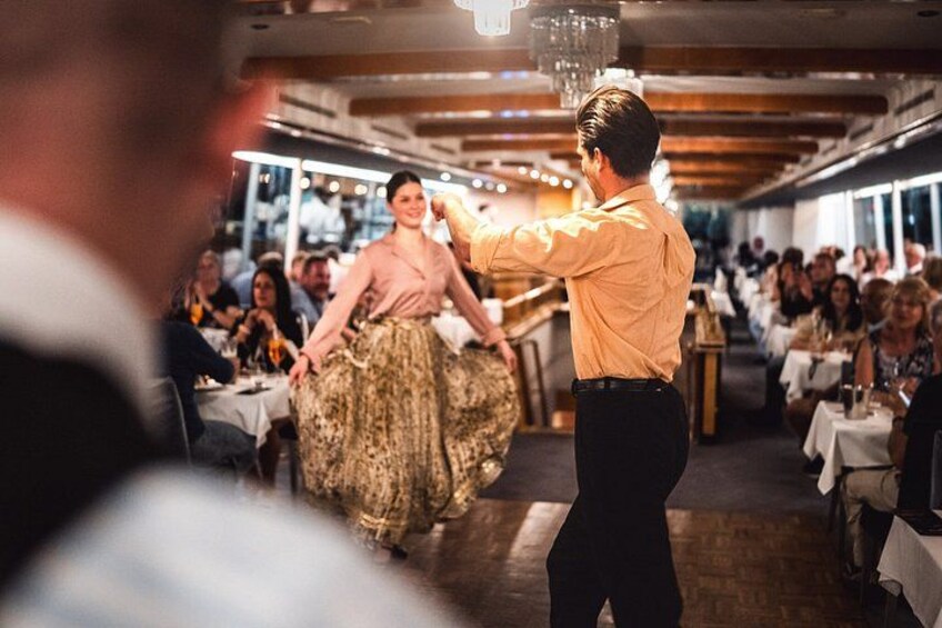 A man in a yellow shirt serving food to a woman in a patterned dress in a restaurant with diners. 2