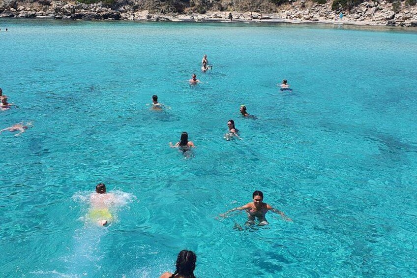 People swimming in a clear blue pool surrounded by rocky terrain. 3