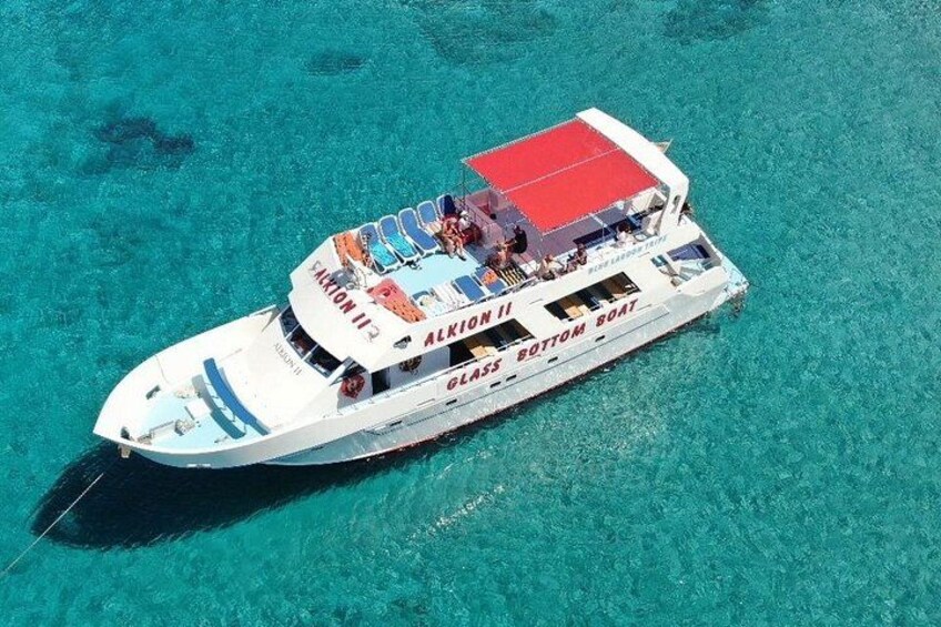 A white boat with a red canopy labeled 'Alkion II' and 'Glacier Bottom Boat' on a clear turquoise sea. 2