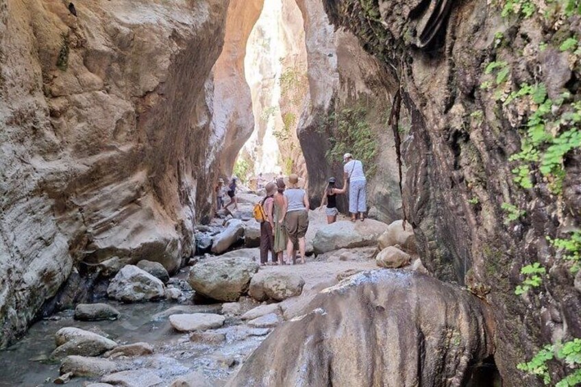 A canyon with a narrow stream, rocky terrain, and people hiking. 3