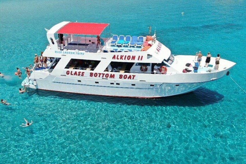 A glass-bottom boat named 'ALKION II' with people on board and others swimming in the clear blue water. 5