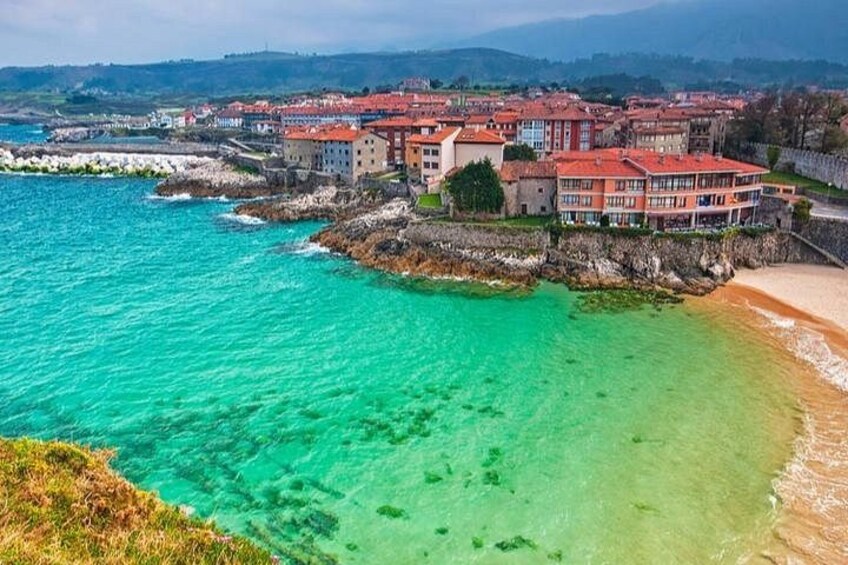 A coastal town with buildings along the shore, clear turquoise water, and a sandy beach. 3