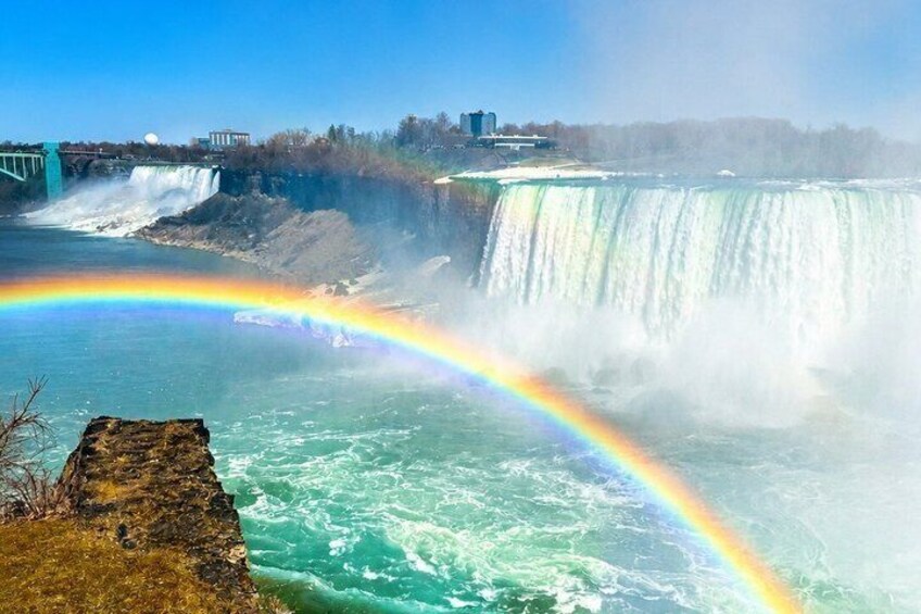 A waterfall with a rainbow, a rocky outcrop, and a bridge in the background. 2