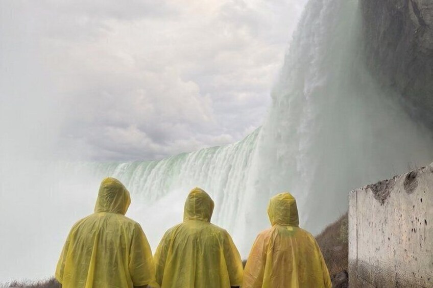 Three people in yellow raincoats observing a waterfall. 3