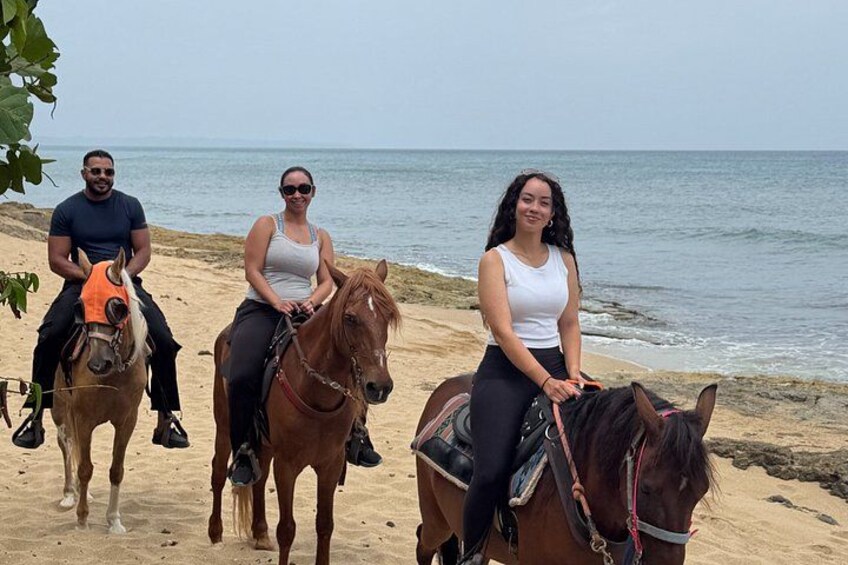 Three people riding horses on a sandy beach with the ocean in the background. 4